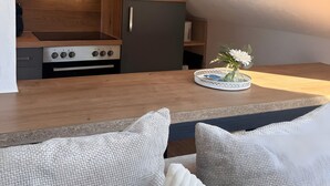 Moderni keittiö, jossa on sisäänrakennettu uuni ja mikroaaltouuni, puinen työtaso sekä pieni ruokailutila, jossa on pöytä ja tuolit.