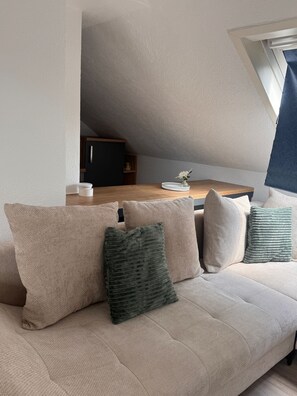 Ein gemütliches Schlafzimmer im Loft-Stil mit schrägverdeckter Decke, einem Holztisch und einer Couch mit Kissen.