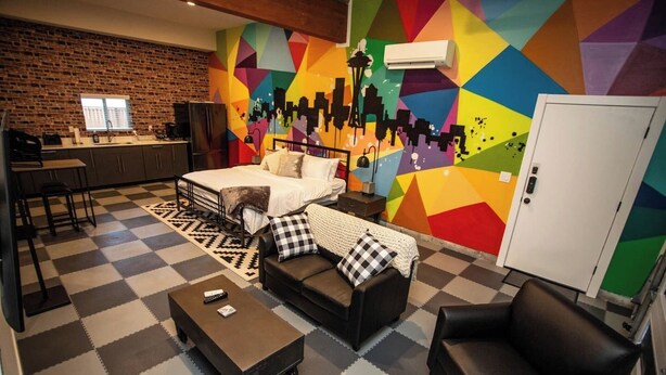 A room with a bed, a sofa, a coffee table, a TV, a kitchen area, and a colorful geometric wall. - Studio with AC in charming Seattle neighborhood (Seattle)