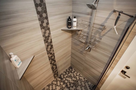 A modern shower area with a glass door, a showerhead, and a shelf with toiletries.. Studio with AC in charming Seattle neighborhood