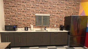 A kitchen with a brick wall, a window with blinds, a microwave, a coffee maker, a sink, and a refrigerator. - Studio with AC in charming Seattle neighborhood (Seattle)