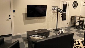 A modern living room with a flat-screen TV, a sofa, a coffee table, a dartboard, and a small dining area. - Studio with AC in charming Seattle neighborhood (Seattle)