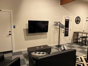 Een moderne woonkamer met een flatscreen televisie, een bank, een salontafel, een dartbord en een kleine eethoek.