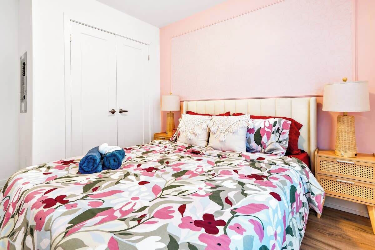 A bedroom with a bed, two bedside tables, a door, and a wall with a floral pattern.