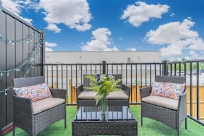 A rooftop patio with wicker furniture, a glass table, and a vase with flowers. - Patio Suite with BBQ & Outdoor Relaxation, Near Niagara Falls! (Niagara Falls)