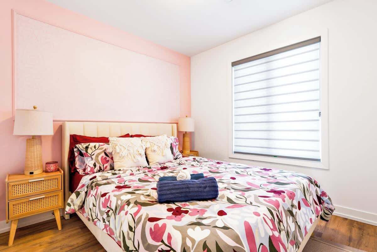 Un dormitorio con cama, mesitas de noche, una ventana con persianas y una pared con textura.