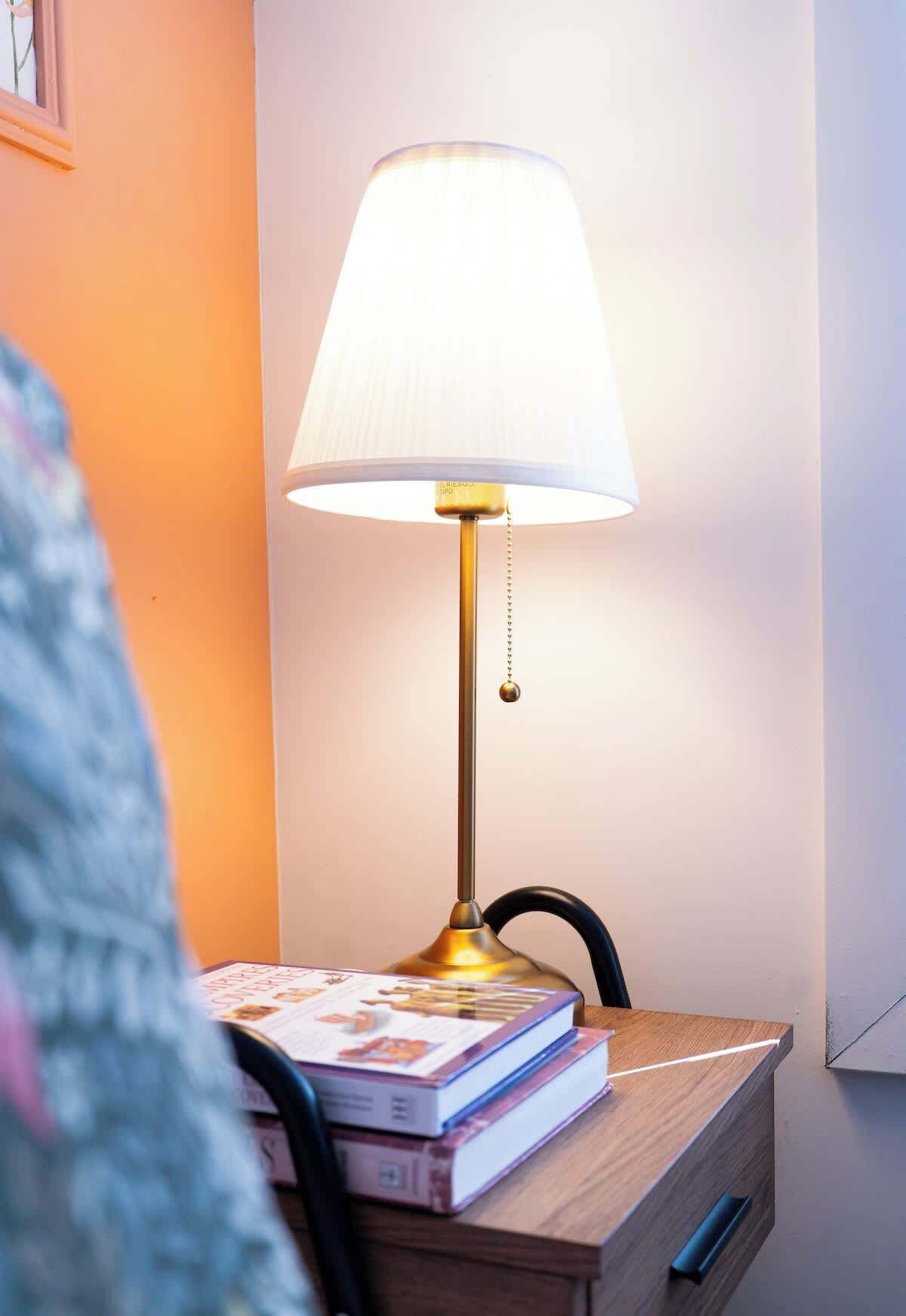 Ett sidobord med en lampa, böcker och en stol.