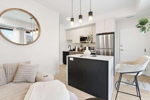 A modern kitchen with white cabinets, a central island, and stainless steel appliances. - Spacious 2-Bedroom Suite, Mins to the Falls, Parking & Sleeps 5! (Niagara Falls)