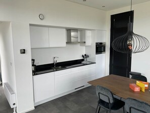 Een moderne keuken met witte kasten, een zwart aanrecht en een eethoek met een houten tafel en stoelen.