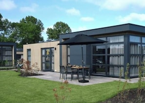 Een modern gebouw met grote ramen, een terras met buitenmeubels en een verzorgd gazon.