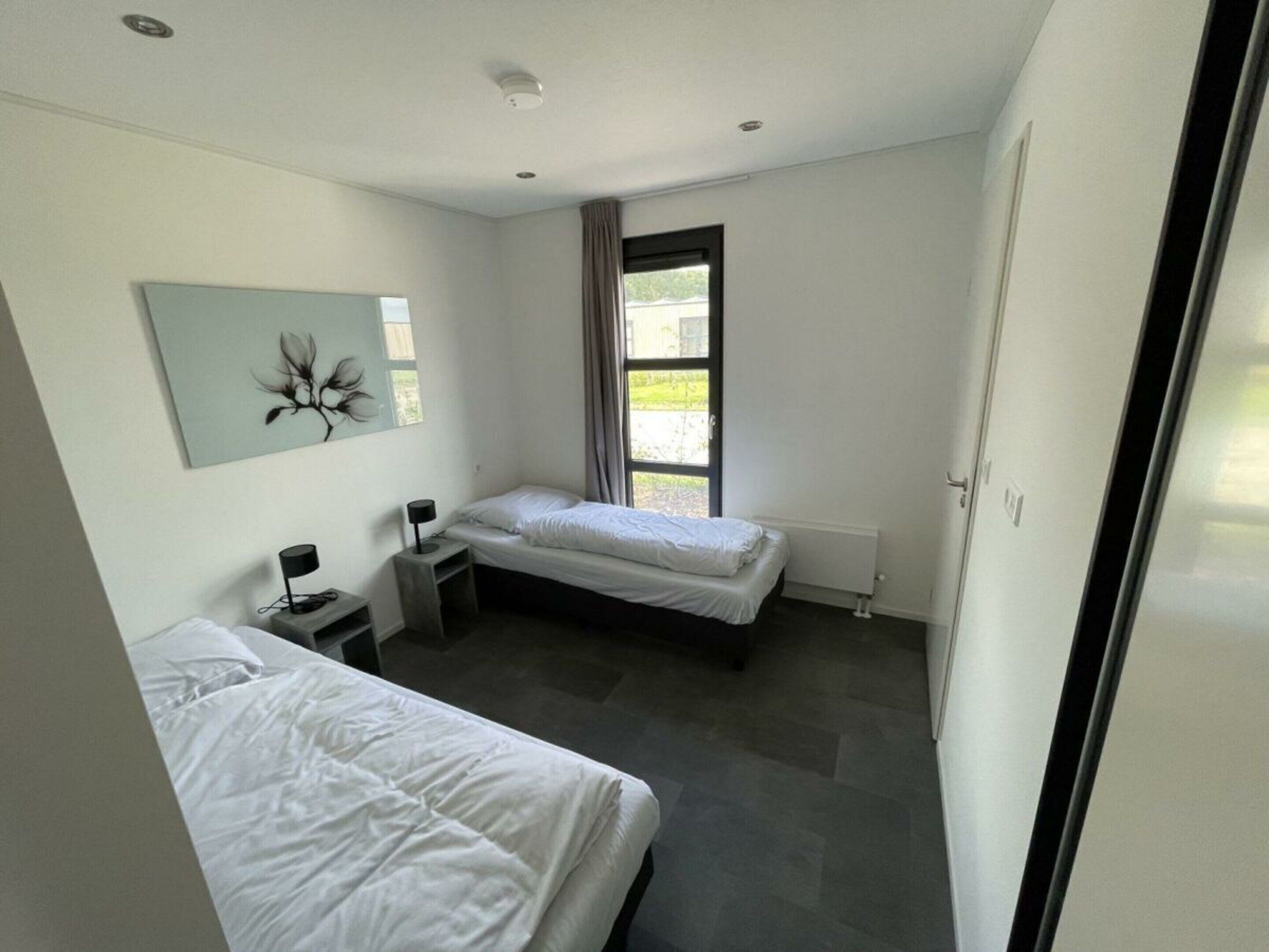 A modern bedroom with two beds, a desk, a chair, and a window with curtains.