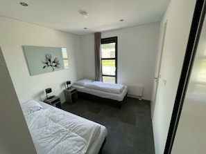 A modern bedroom with two beds, a desk, a chair, and a window with curtains.