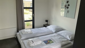 Habitación de hotel con dos camas, una ventana con cortinas, una mesita de noche con lámpara y una obra de arte colgada en la pared.
