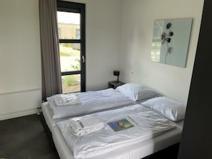 Een hotelkamer met twee bedden, een raam met gordijnen, een nachtkastje met lamp en een kunstwerk aan de muur.