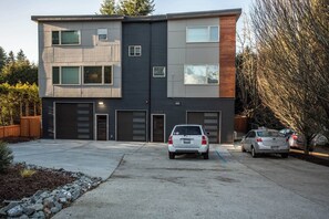 Un edificio moderno de dos plantas con garaje, entrada para vehículos y dos coches estacionados.