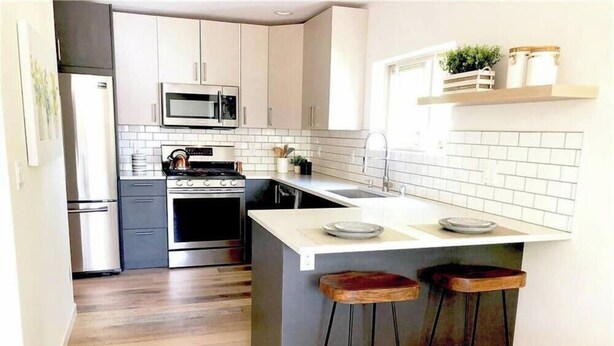 Een moderne keuken met witte kasten, een roestvrijstalen koelkast, een magnetron, een oven, een spoelbak en een bar met barkrukken.
