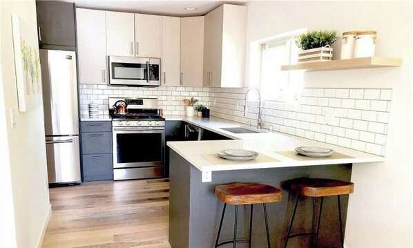 Une cuisine moderne avec des meubles blancs, un réfrigérateur en acier inoxydable, un four à micro-ondes, un four traditionnel, un évier et un coin bar avec des tabourets.