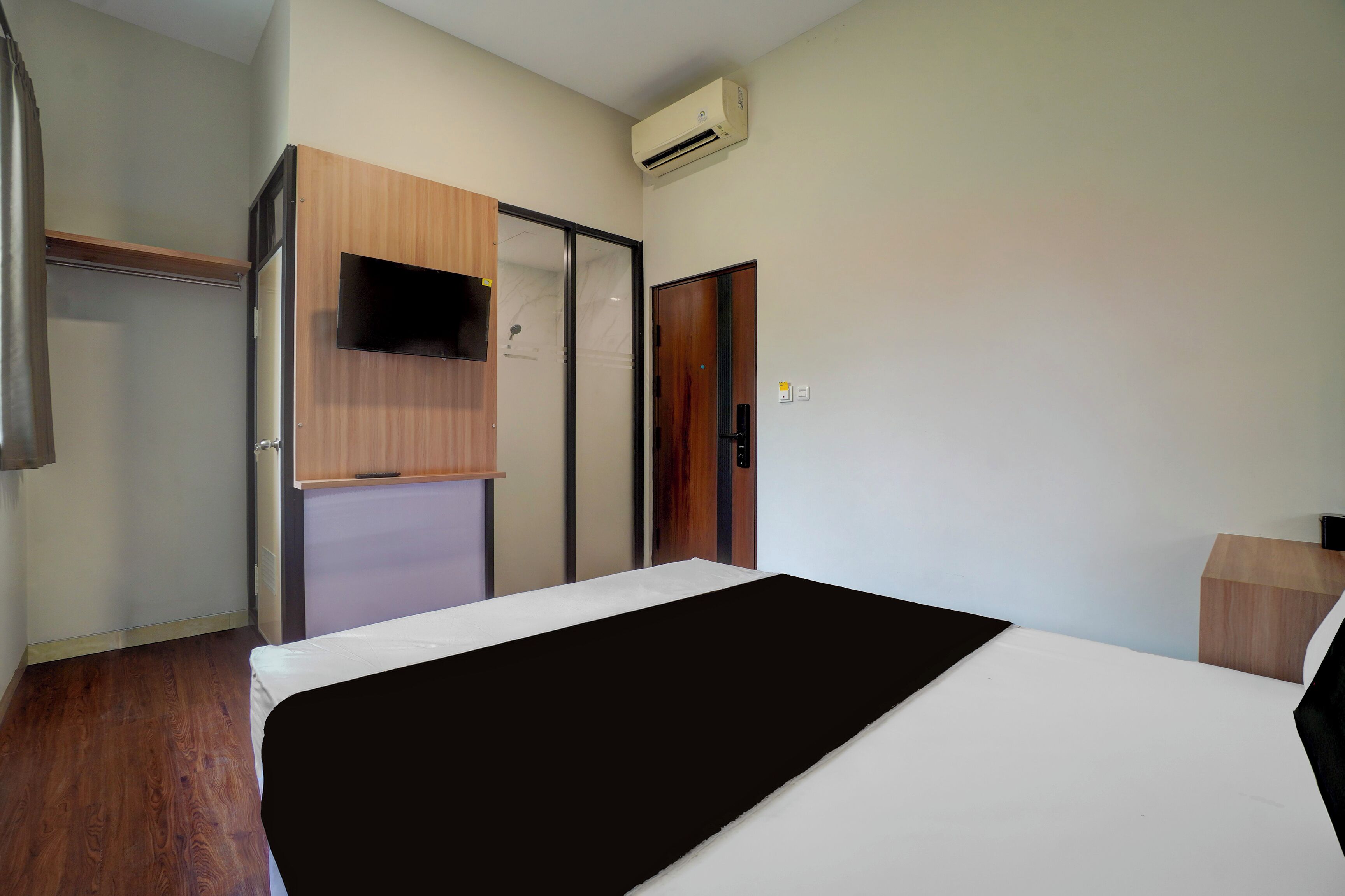 A bedroom with a bed, a wardrobe, a television, and an air conditioning unit.