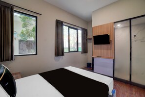 Quarto de hotel com cama, televisão fixada na parede e porta deslizante para a área do chuveiro.
