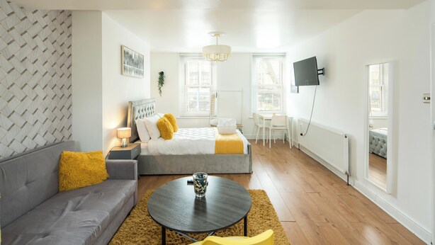 Un dormitorio moderno con cama, sofá y televisor montado en la pared.