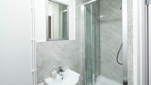 Un baño con lavabo, espejo y ducha con mampara de vidrio.