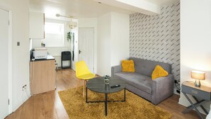 Una sala de estar moderna con sofá, una mesa de centro, un sillón amarillo, una pequeña cocina y una pared con diseño.
