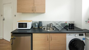 Cocina pequeña equipada con microondas, tostadora, hervidor de agua, lavabo y lavadora.