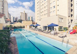 A swimming pool with lounge chairs and umbrellas, surrounded by high-rise buildings. - Modern apartment in Vila Olímpia near Av. Faria Lima with a pool and fitness center (São Paulo)