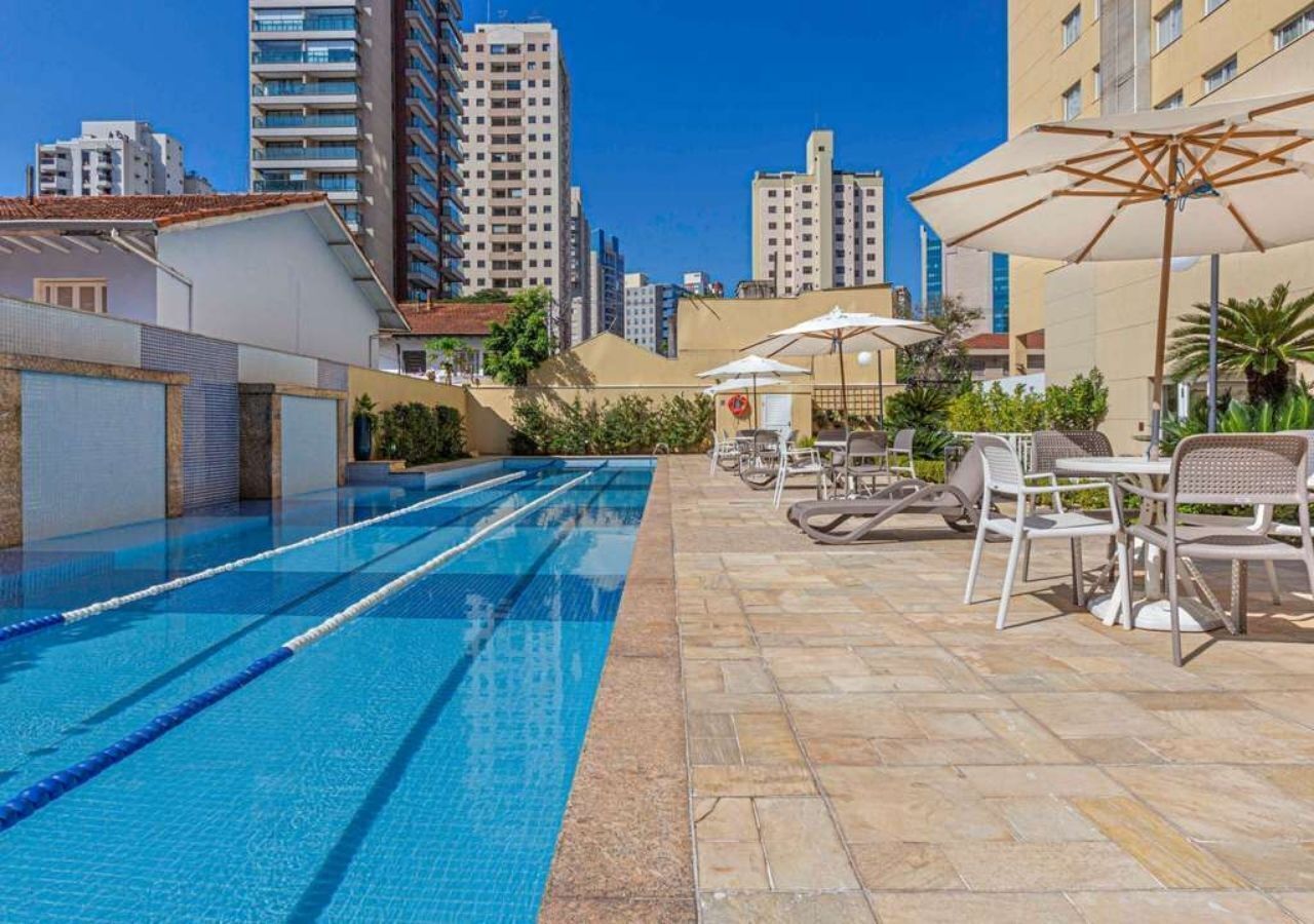 Une piscine entourée de bâtiments, avec des chaises longues et des parasols.