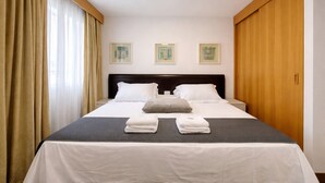 Ein Hotelzimmer mit Bett, Vorhängen, einem Kopfteil und drei gerahmten Bildern an der Wand.