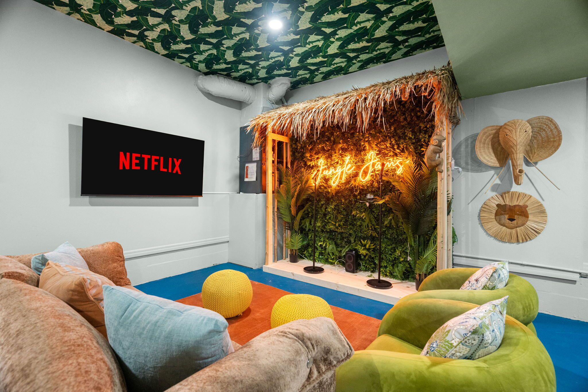 Una habitación con un cartel de Netflix, un muro de paja y diferentes opciones de asiento, incluyendo una silla verde y un sofá.