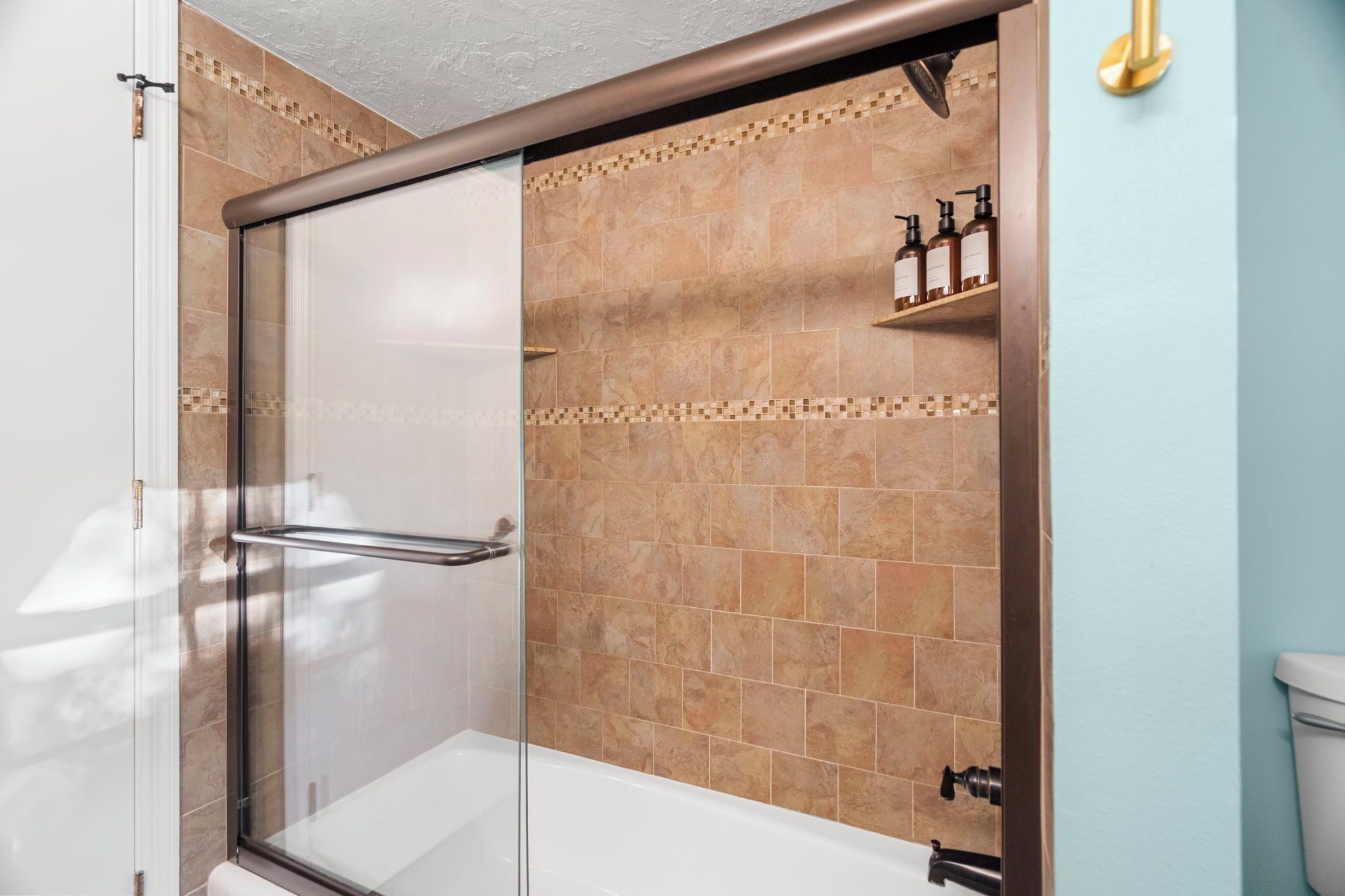 A shower with a glass door, a white bathtub, and a tiled wall with a patterned border.