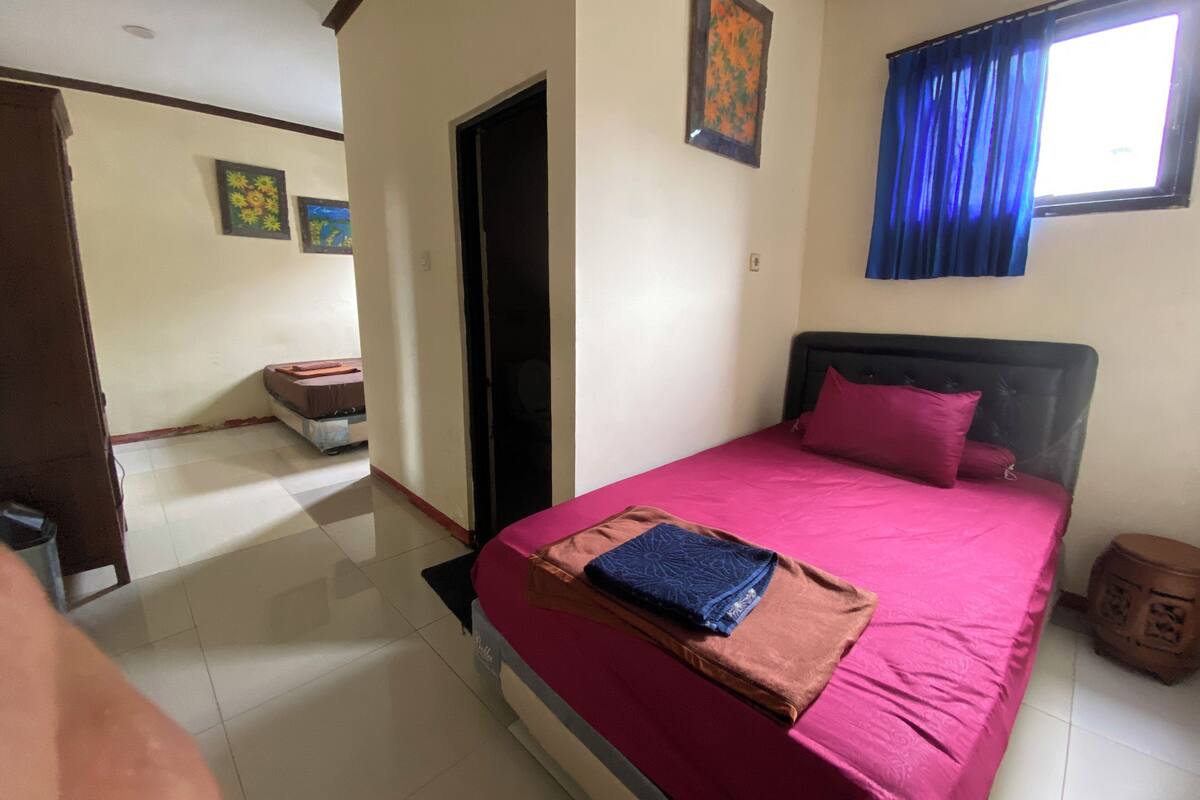 Quarto com cama, porta, janela com cortinas azuis e parede com duas molduras.