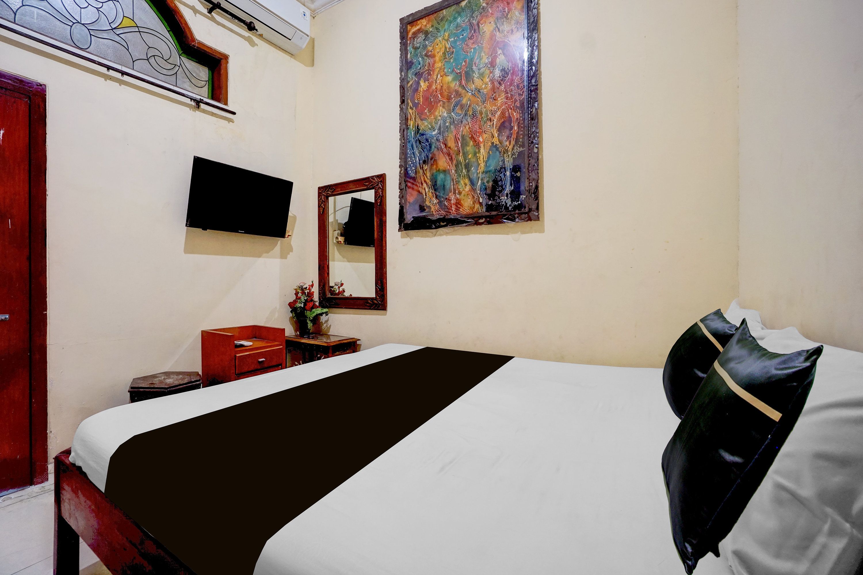 A hotel room with a bed, a flat-screen TV, a painting, and a mirror.