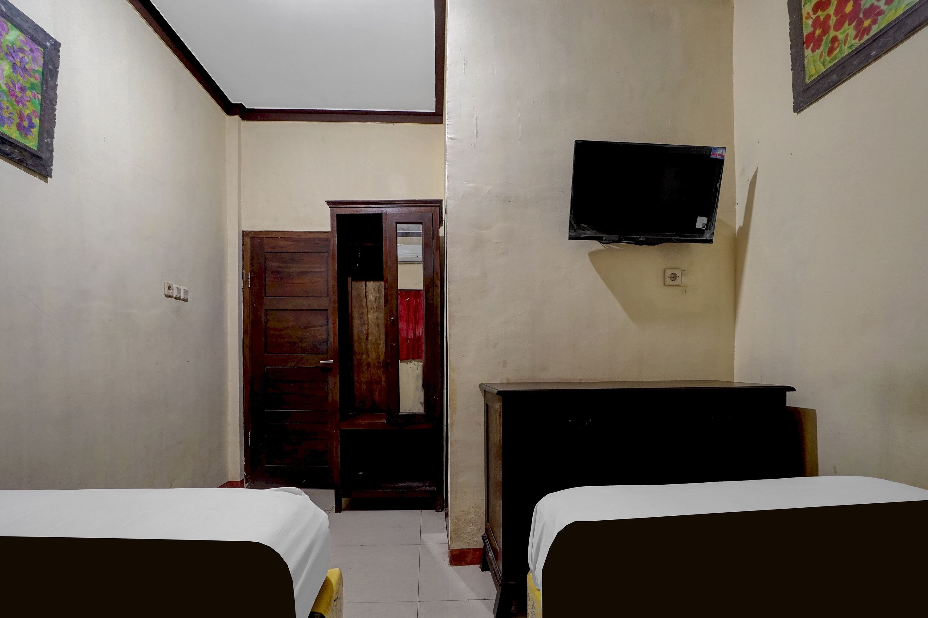 A room with two beds, a television on the wall, and a door leading to another room.