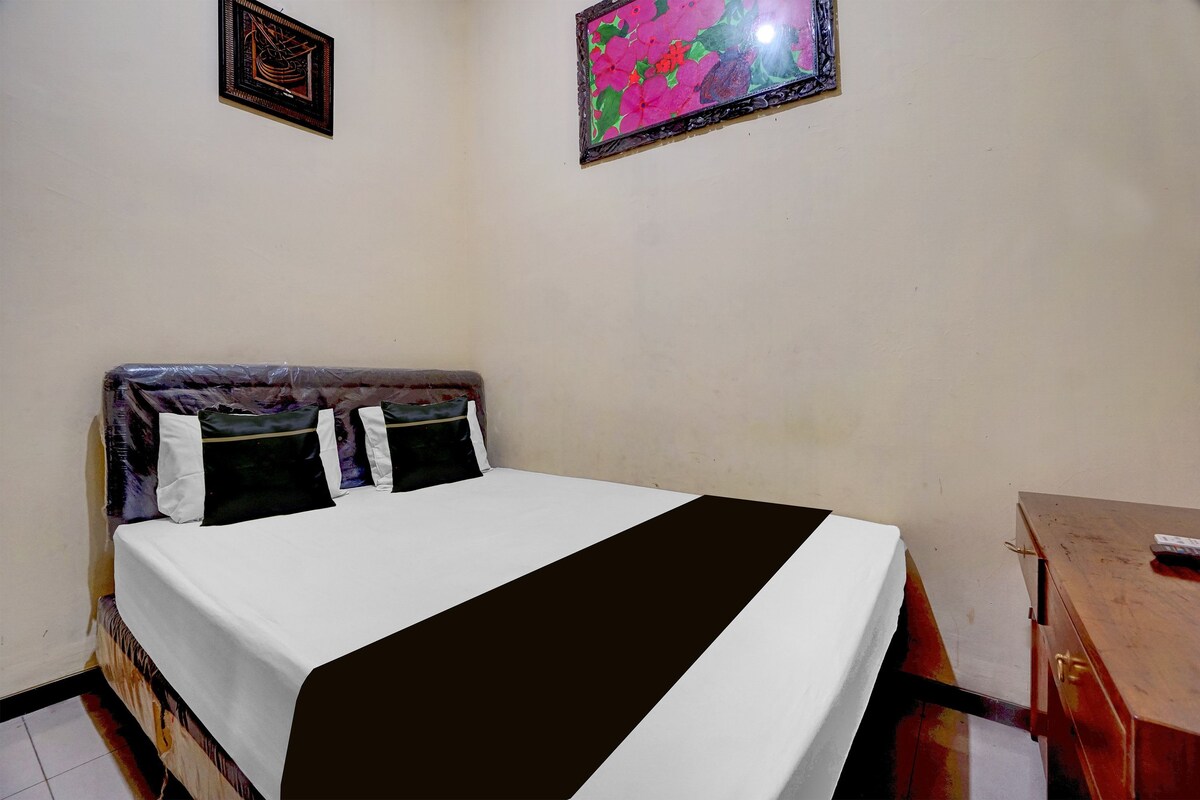 A bed with a white mattress, black and white pillows, and a brown headboard. There is a wooden nightstand to the right of the bed.