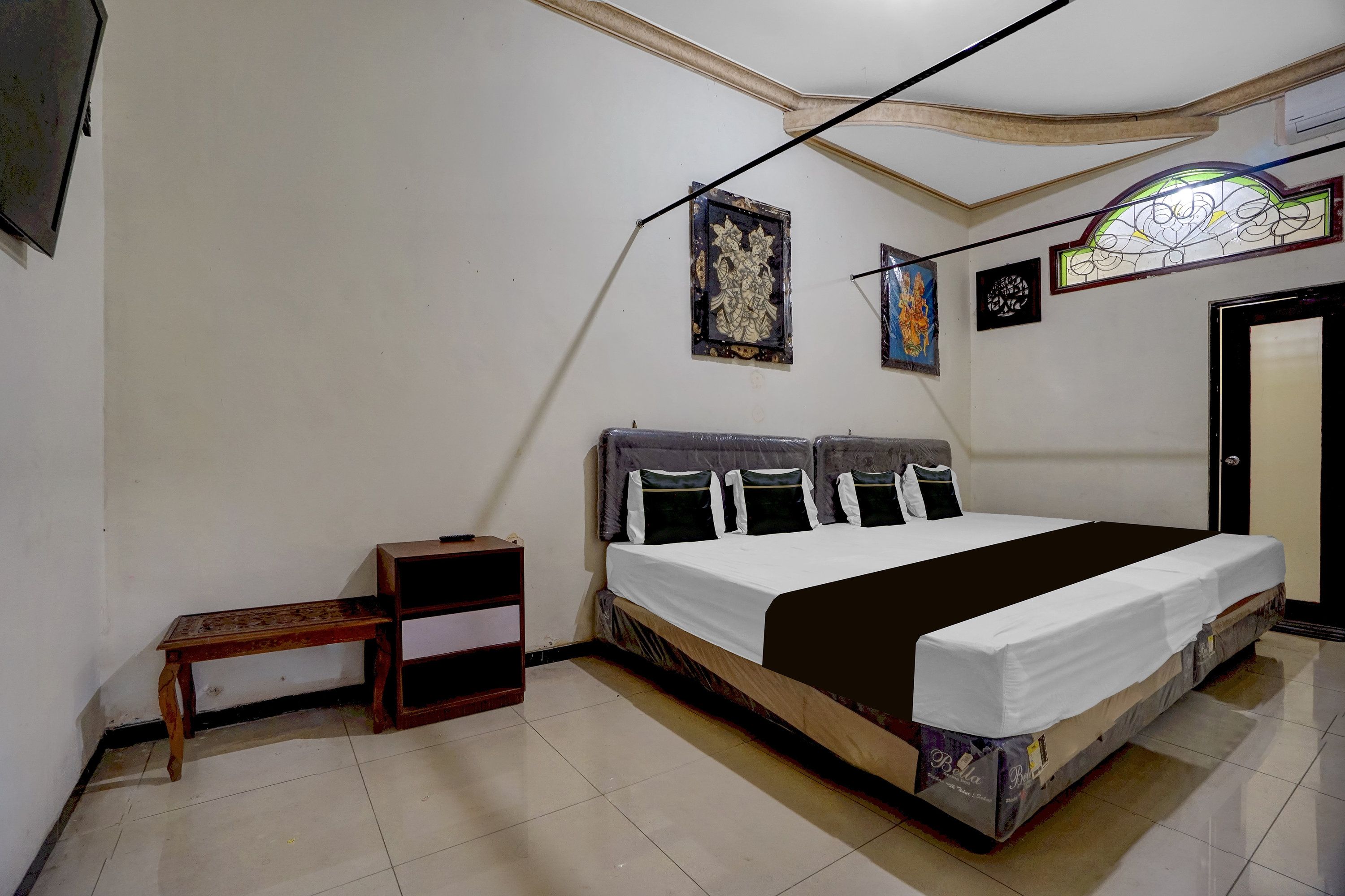 A bedroom with a bed, a nightstand, a wall-mounted shelf, and a door.
