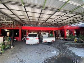 A covered car wash facility with two cars and a truck, potted plants, and a red building facade. - Hotel O near City of Tomorrow Mall forme (Surabaya)