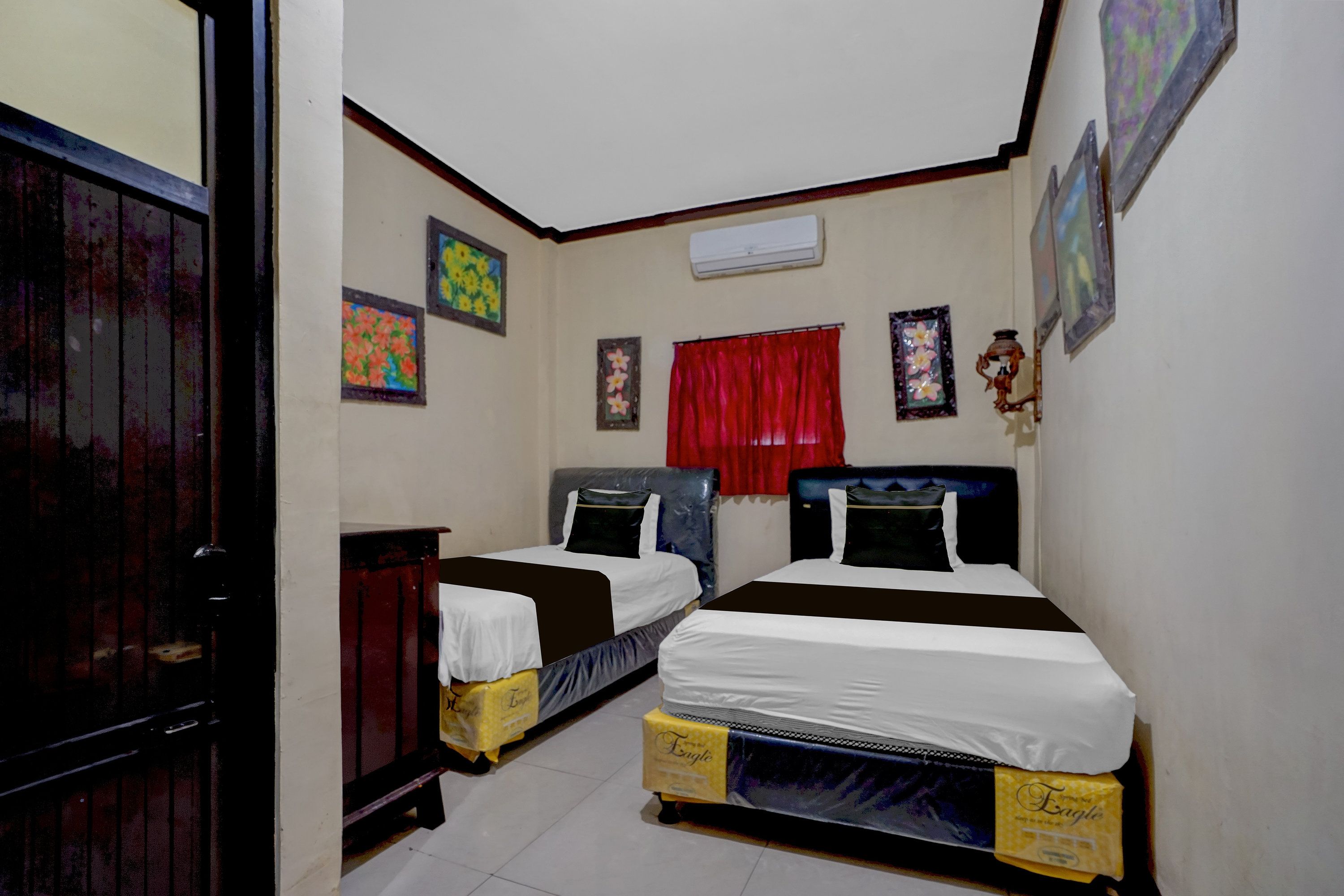 A room with two beds, a red curtain, and wall art.