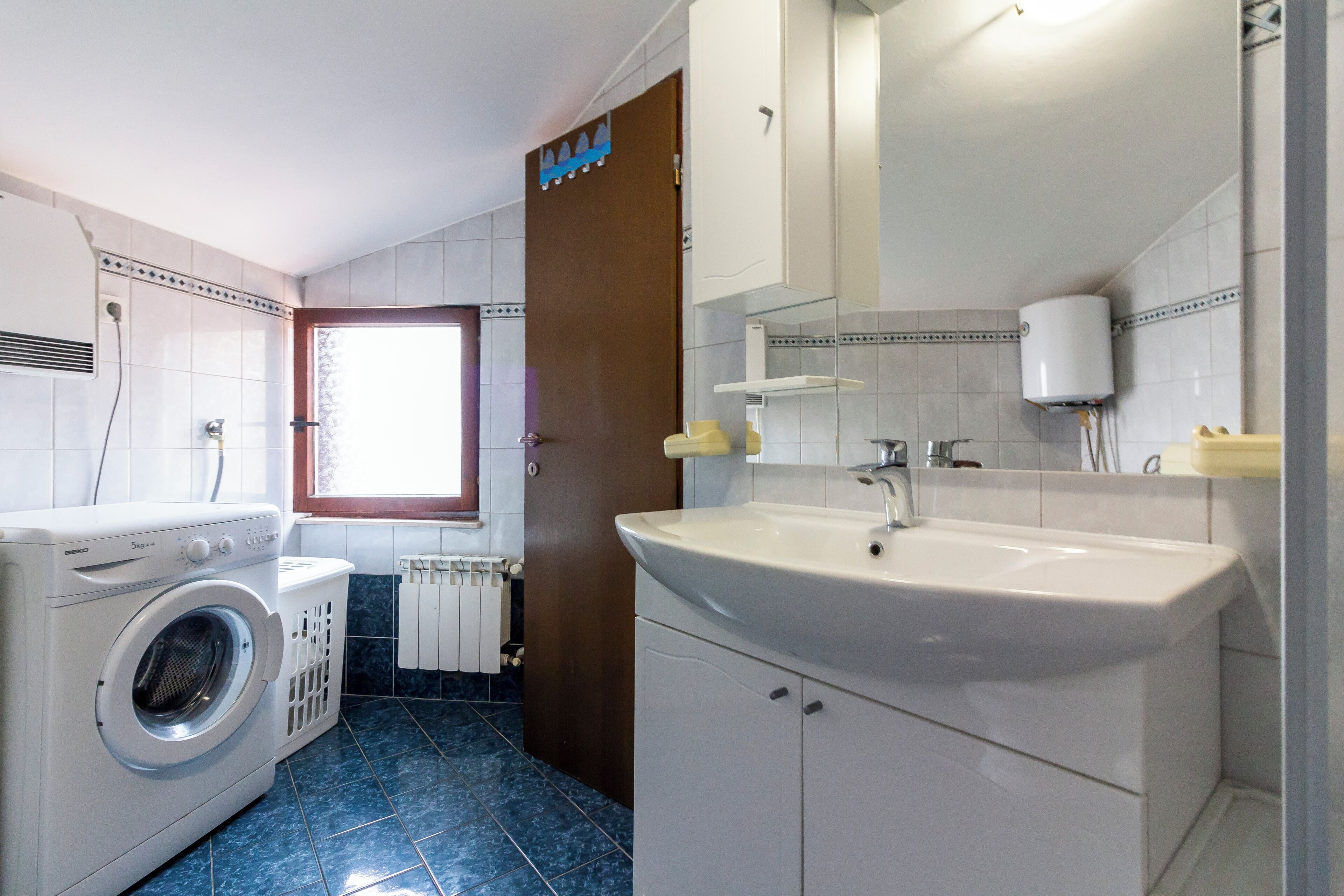 A laundry area with a washing machine, a sink with a mirror above, and a window with a view.