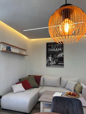 Ein modernes Wohnzimmer mit einem Ecksofa, einem Holztisch, einer hängenden orangefarbenen Pendelleuchte und einem motivierenden Poster an der Wand.