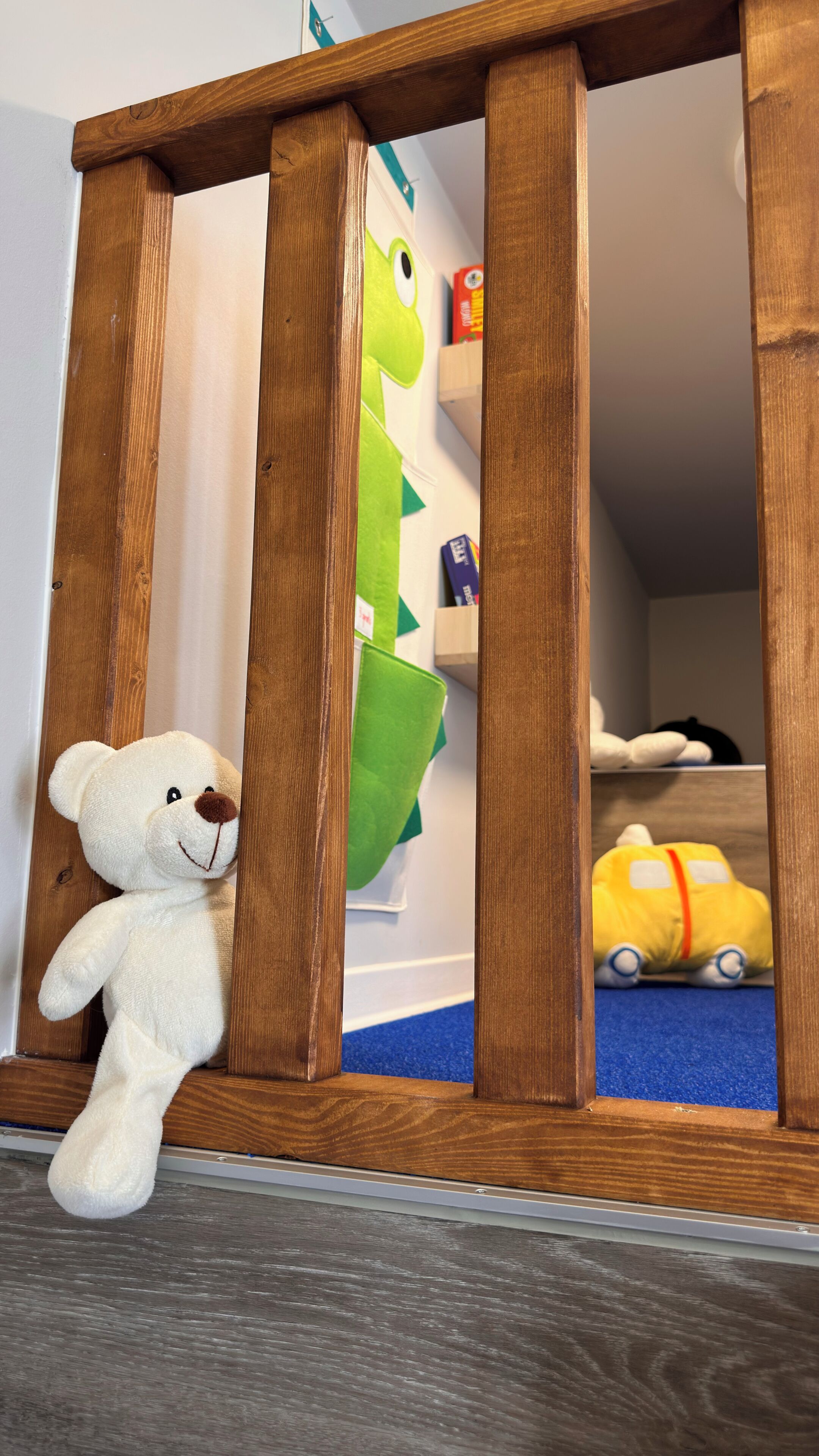 A wooden playpen with a white teddy bear leaning against it, a green toy, and a yellow toy inside.