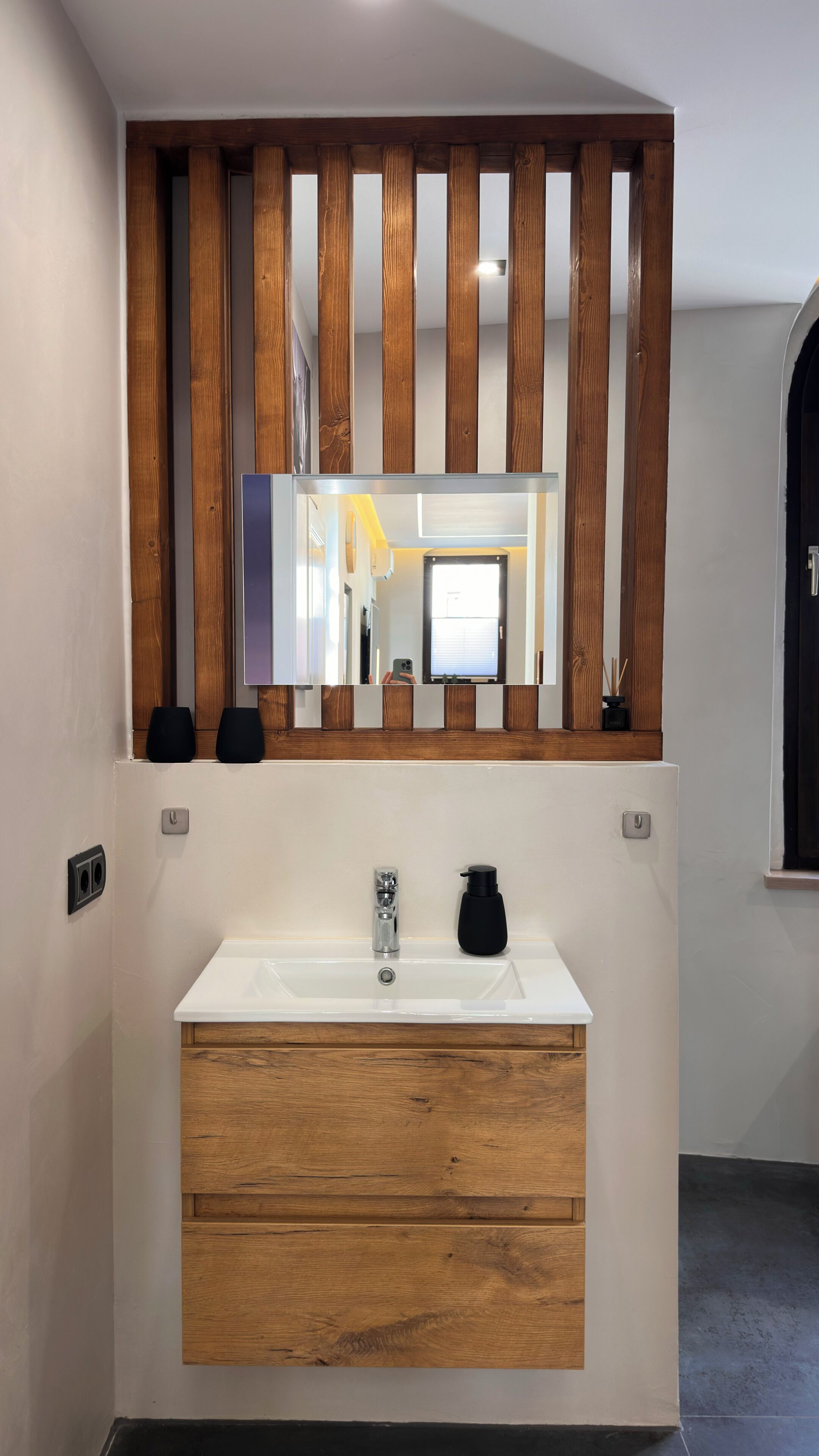 A modern bathroom with a wooden vanity, a white sink, and a mirror above.