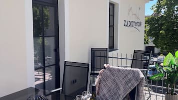 An outdoor dining area with a table set for two, chairs, a potted plant, and a building with a sign reading 'zur promenade apartments'.