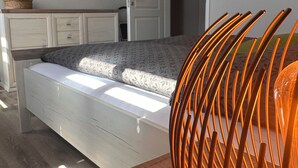 Een slaapkamer met een bed, een aan de muur bevestigde televisie, een kledingkast en een deur naar een andere kamer.