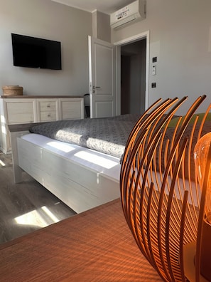 Une chambre à coucher comprenant un lit, un téléviseur fixé au mur, une armoire et une porte donnant sur une autre pièce.
