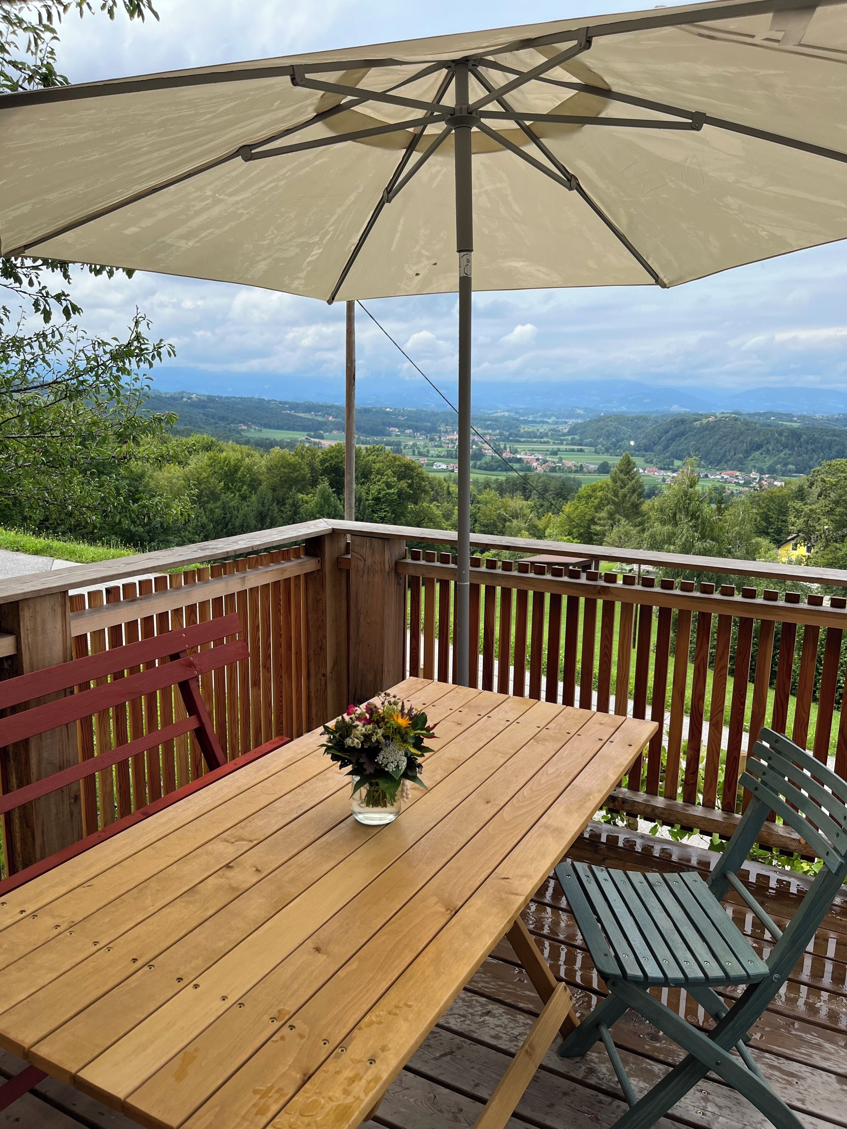 Una terraza de madera con una mesa, sillas y una sombrilla, con vistas a un paisaje.