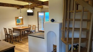 Cuina amb bigues de fusta, zona de menjador amb cadires, una petita illa i una escala.