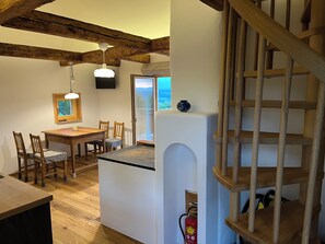 Eine Küche mit Holzbalken, einem Essbereich mit Stühlen, einer kleinen Kochinsel und einer Treppe.