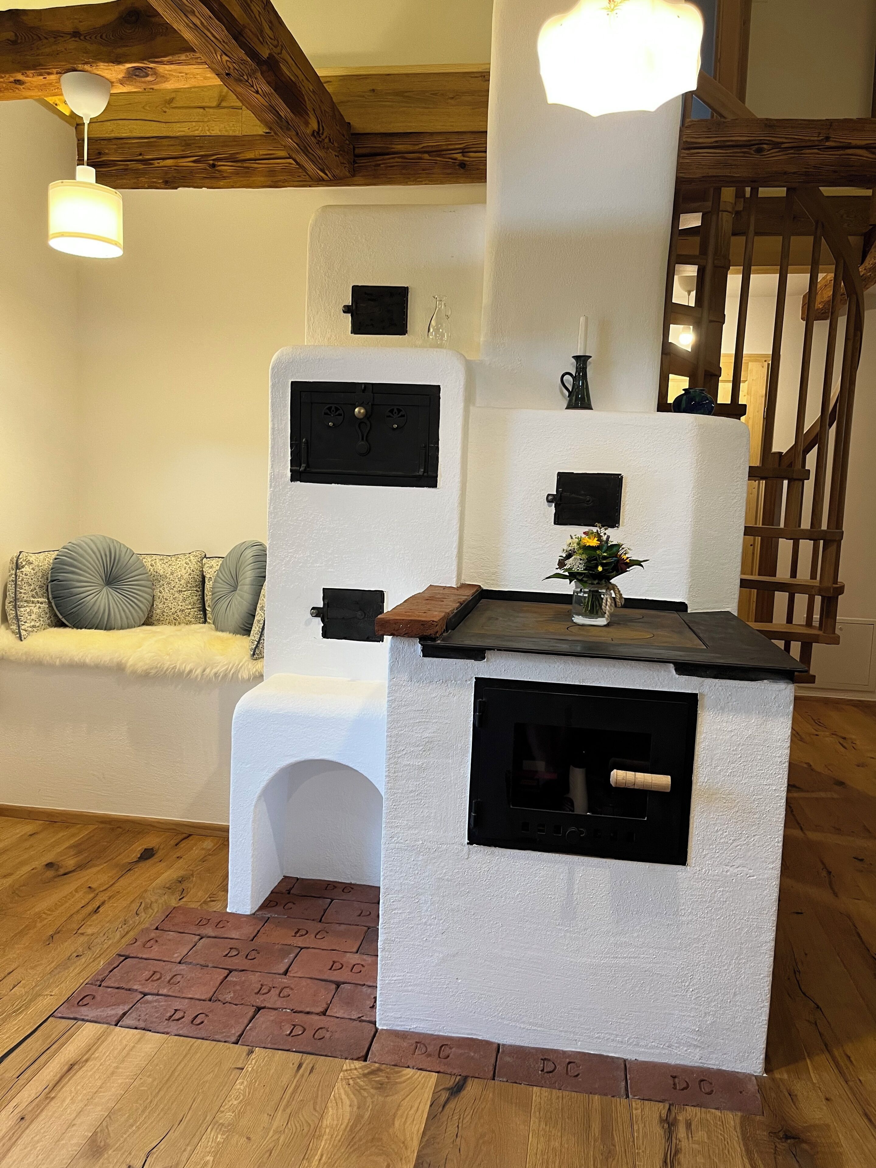 A cozy room with a fireplace, a wooden ceiling, a white bench with cushions, and a brick-patterned floor.